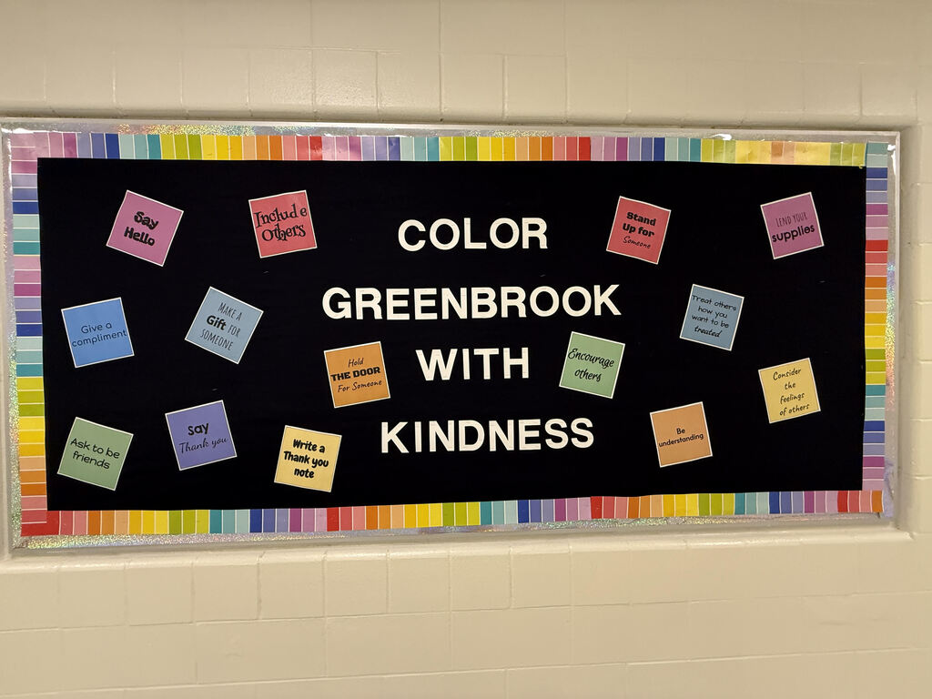 Blackboard with a colorful border displays "COLOR GREENBROOK WITH KINDNESS". Many colorful sticky notes with various messages adorn the board.