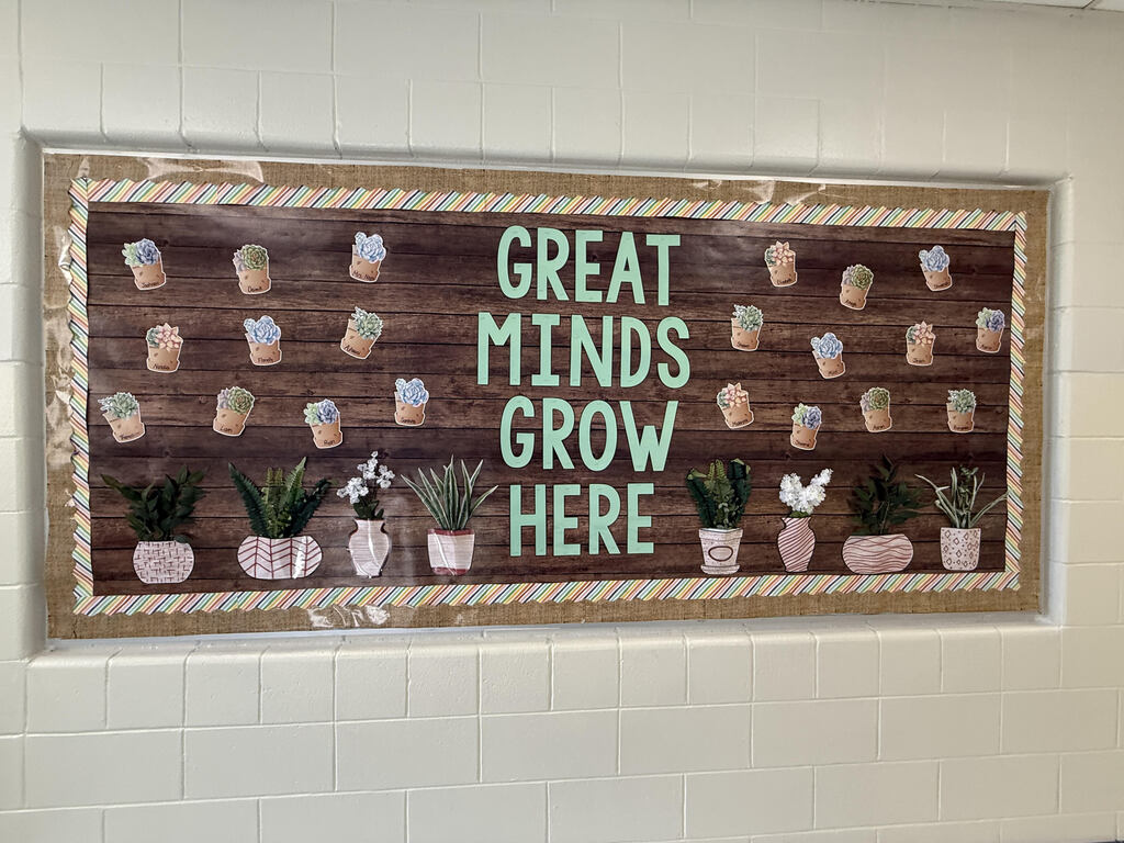A bulletin board displays a wooden background with plants in pots. Words "Great Minds Grow Here" are displayed in green letters.