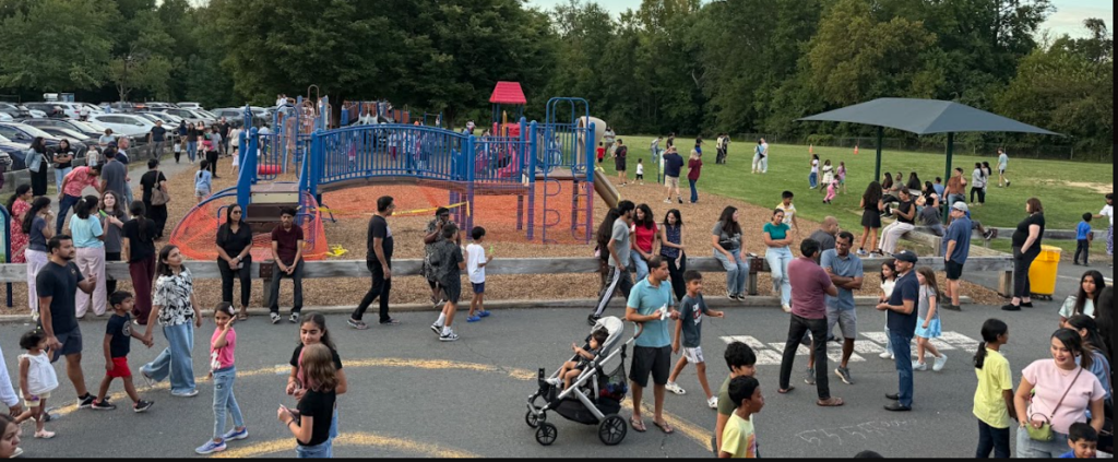 A park with playground equipment, people walking, a stroller, and a canopy. Trees and parked cars visible.