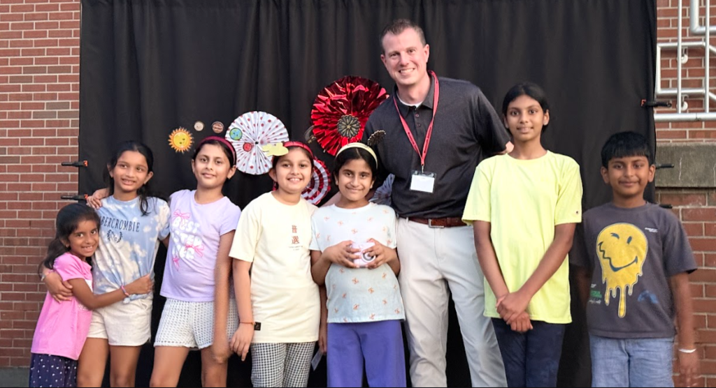 Adults and children pose for a photo in front of a brick wall. Some children wear bracelets.