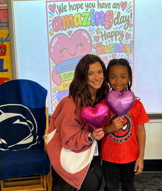 Two people standing next to each other. A woman holds two balloons. A child holds a purple balloon.