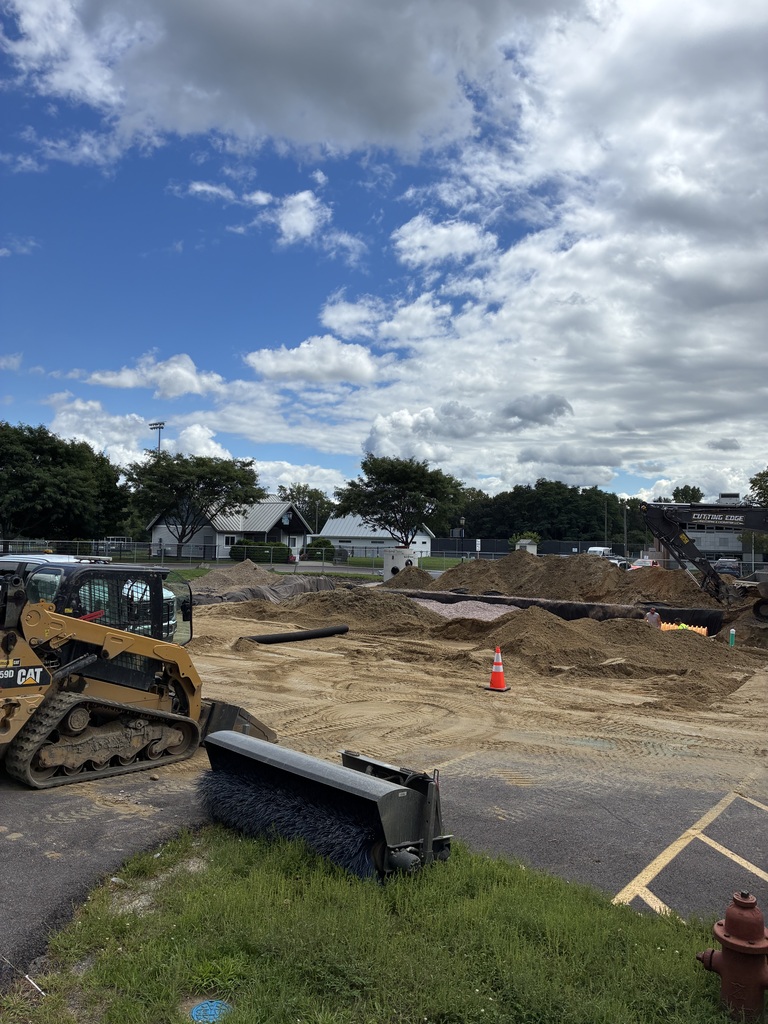 Construction site with a bulldozer and a fire hydrant. Trees and houses in the distance. Bright, cloudy sky overhead.
