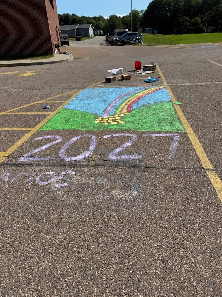 An outdoor area with a chalk drawing of a rainbow and the numbers 2021 on the ground.