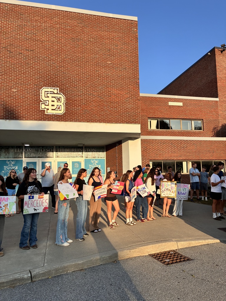 Group of people holding signs in front of a brick building. A logo is on the front of the building.