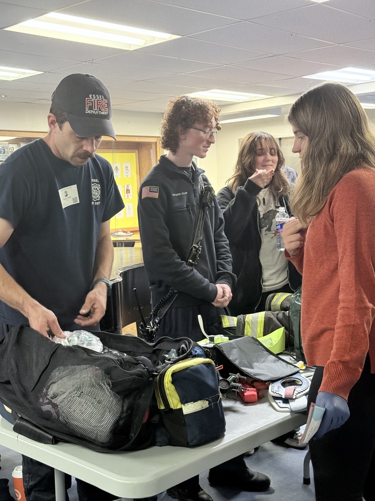Four people in a room with bags on a table. Two men look at items while two women converse.