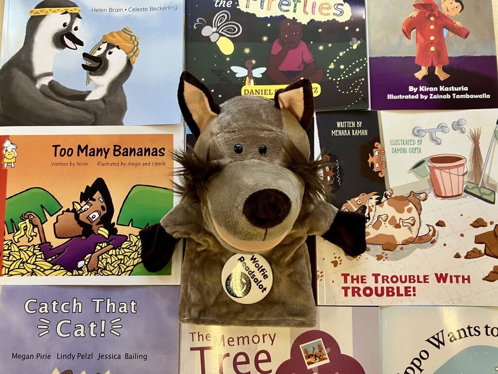 Multiple children's books on a background with a gray puppet of a wolf in the center with a badge.