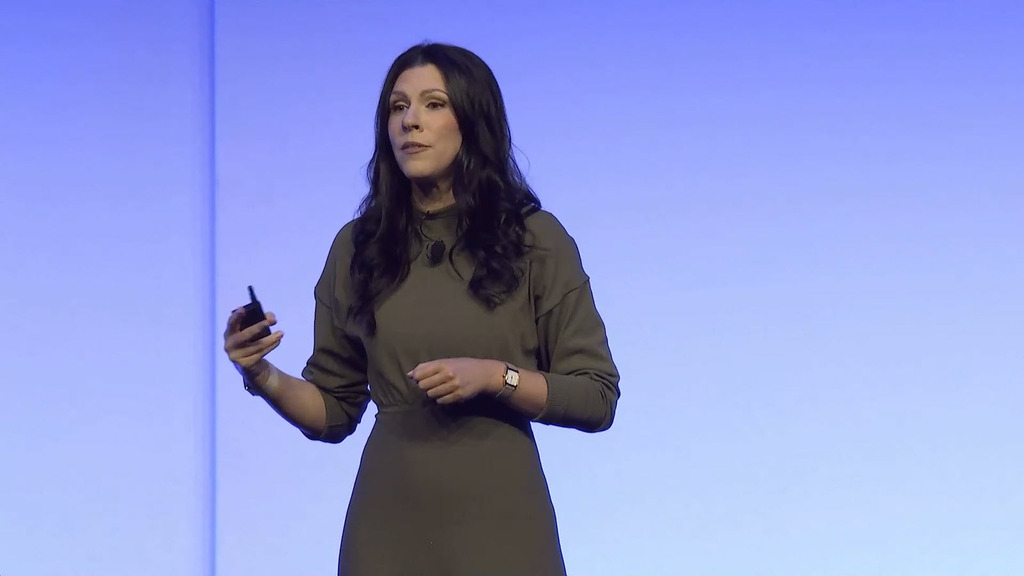 Woman in a green dress wearing a watch on her wrist and holding a black device standing in front of a blue screen