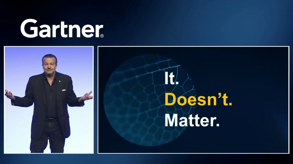 Gartner. Man in a black suit shrugging shoulders with hand held up standing in front of a light blue and white screen. It. Doesn't. Matter. Blue ball in background with pentagons on it.