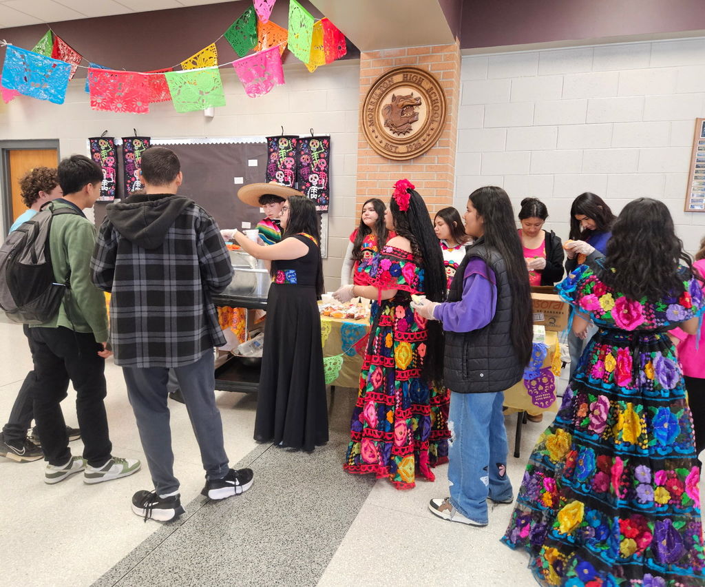 students dressed in traditional Mexican style, serving hot cocoa and sweet bread to other students