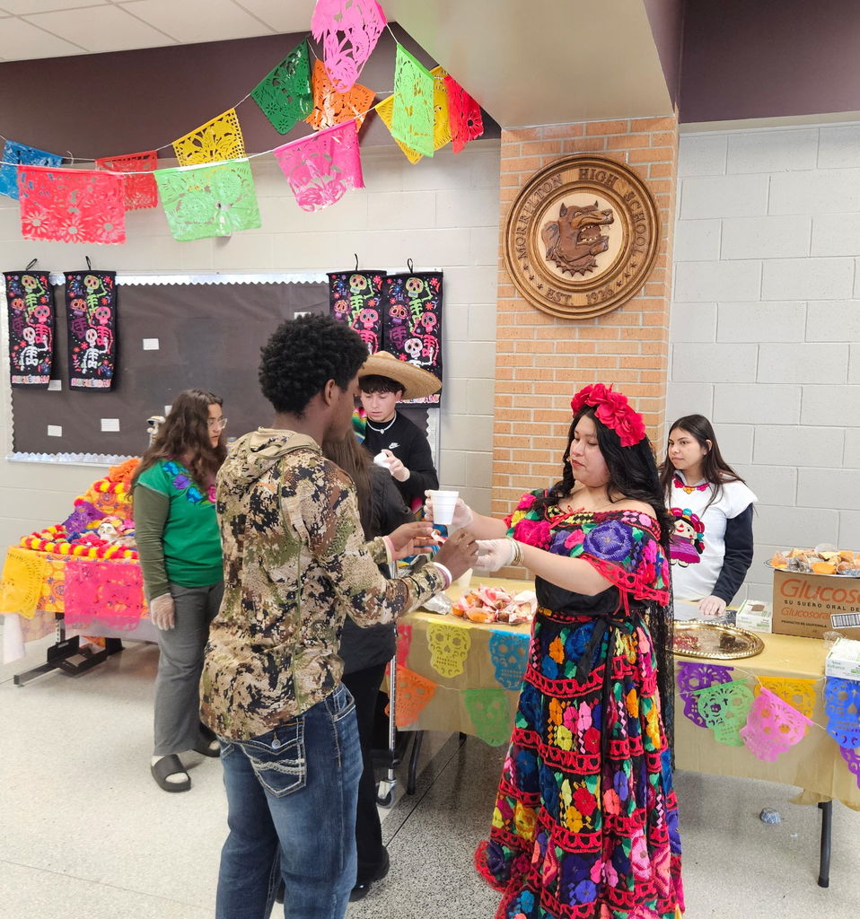 students dressed in traditional Mexican style, serving hot cocoa and sweet bread to other students