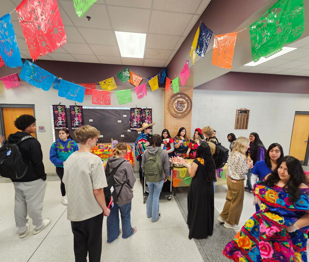 students dressed in traditional Mexican style, serving hot cocoa and sweet bread to other students