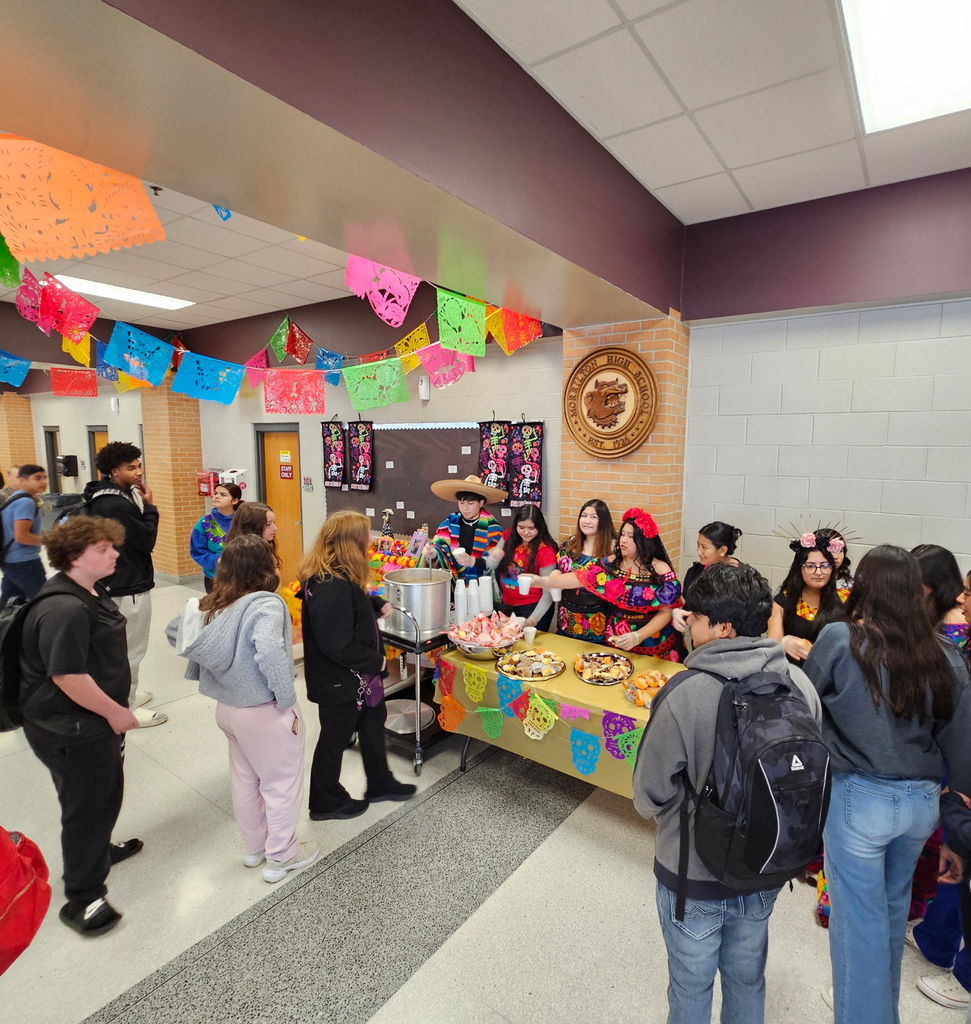 students dressed in traditional Mexican style, serving hot cocoa and sweet bread to other students