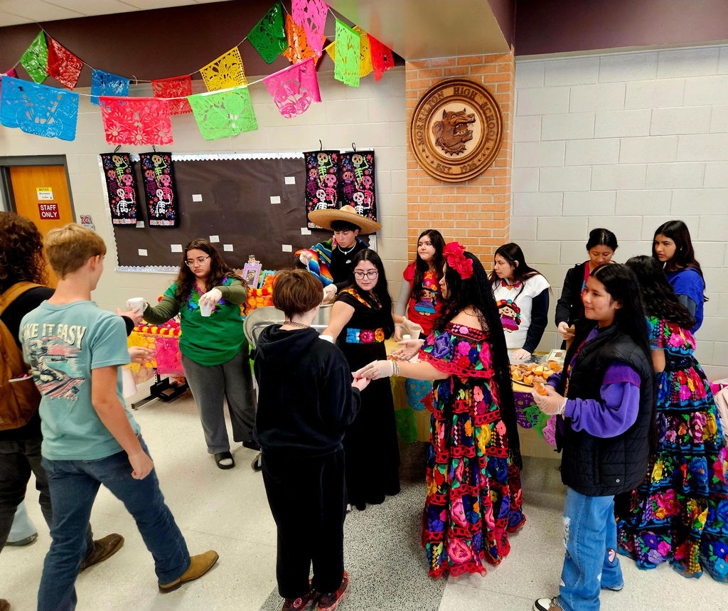 students dressed in traditional Mexican style, serving hot cocoa and sweet bread to other students
