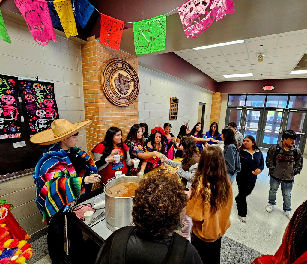 students dressed in traditional Mexican style, serving hot cocoa and sweet bread to other students