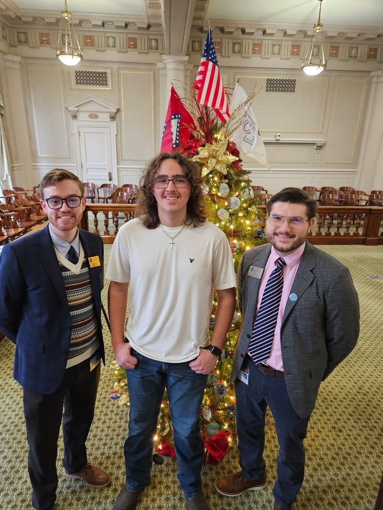 student and 2 men standing in front of a Christmas tree