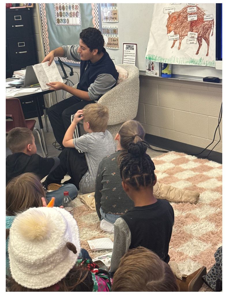 students sitting on a rug listening to student teacher read them a book