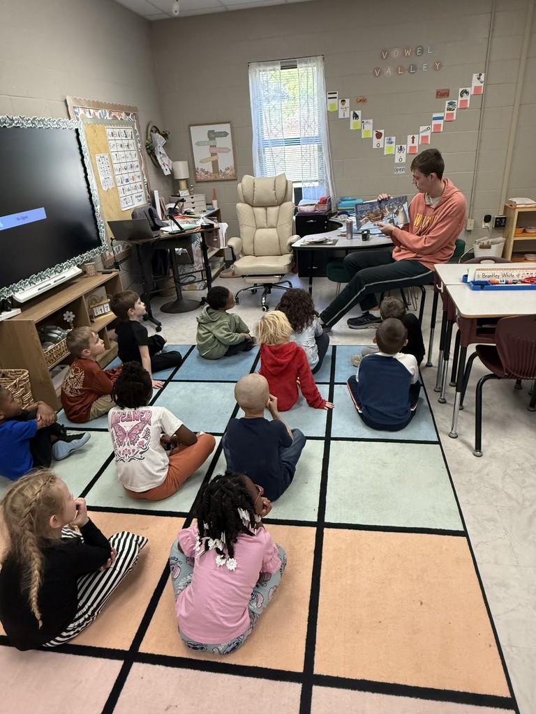 students sitting on rug listening to student teacher read them a book
