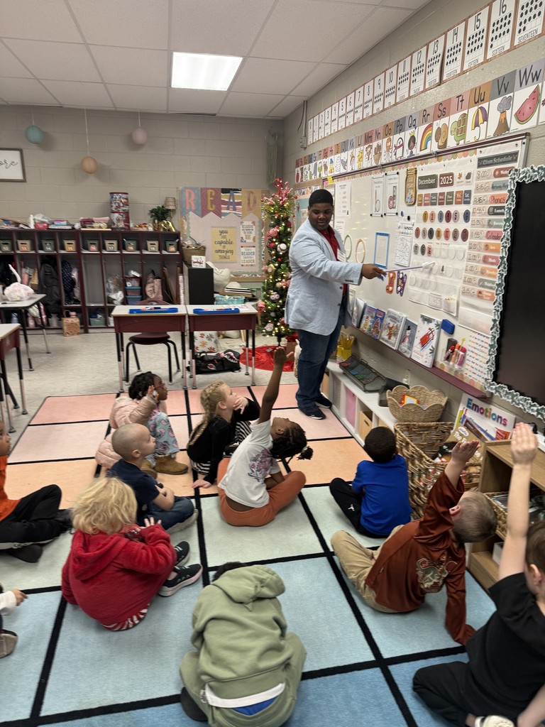students sitting on a rug, participating in a lesson taught by a student teacher