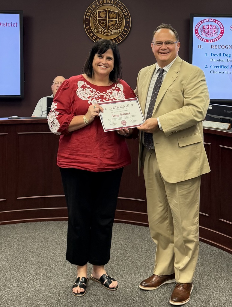 A woman in red stands with a certificate in hand. A man in a suit holds it above her.