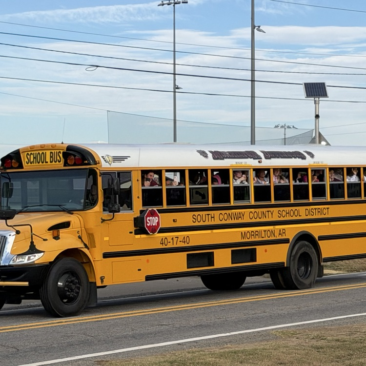 Yellow school bus with many students riding inside, traveling down a paved road.