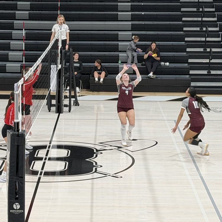 A group of people playing volleyball in a gym with a court marked with a letter B.