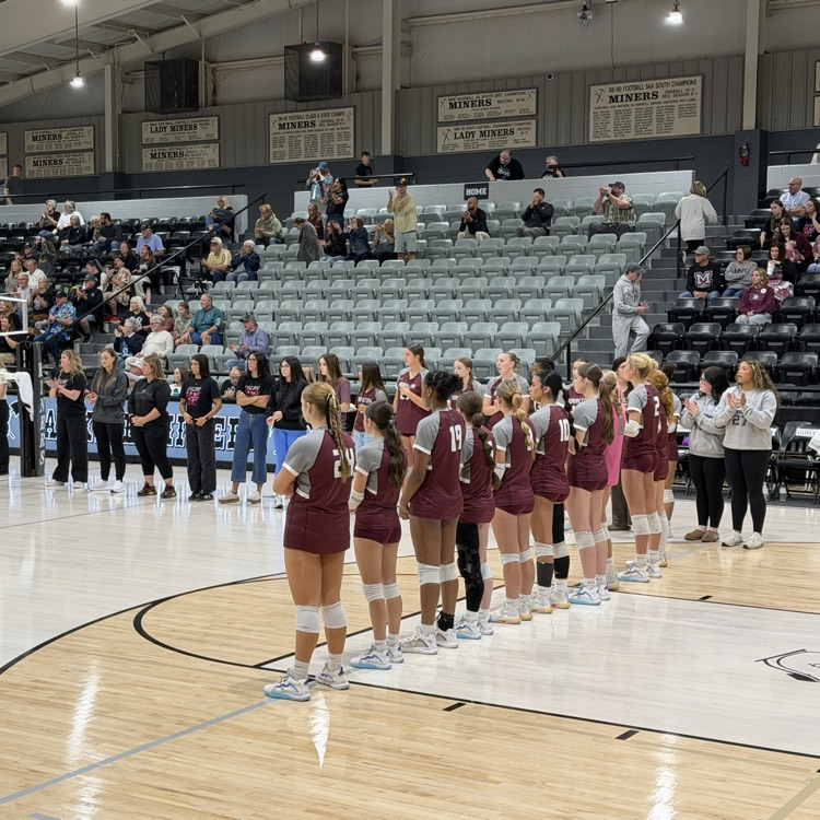 A group of women in maroon uniforms on a basketball court with a crowd seated in bleachers.