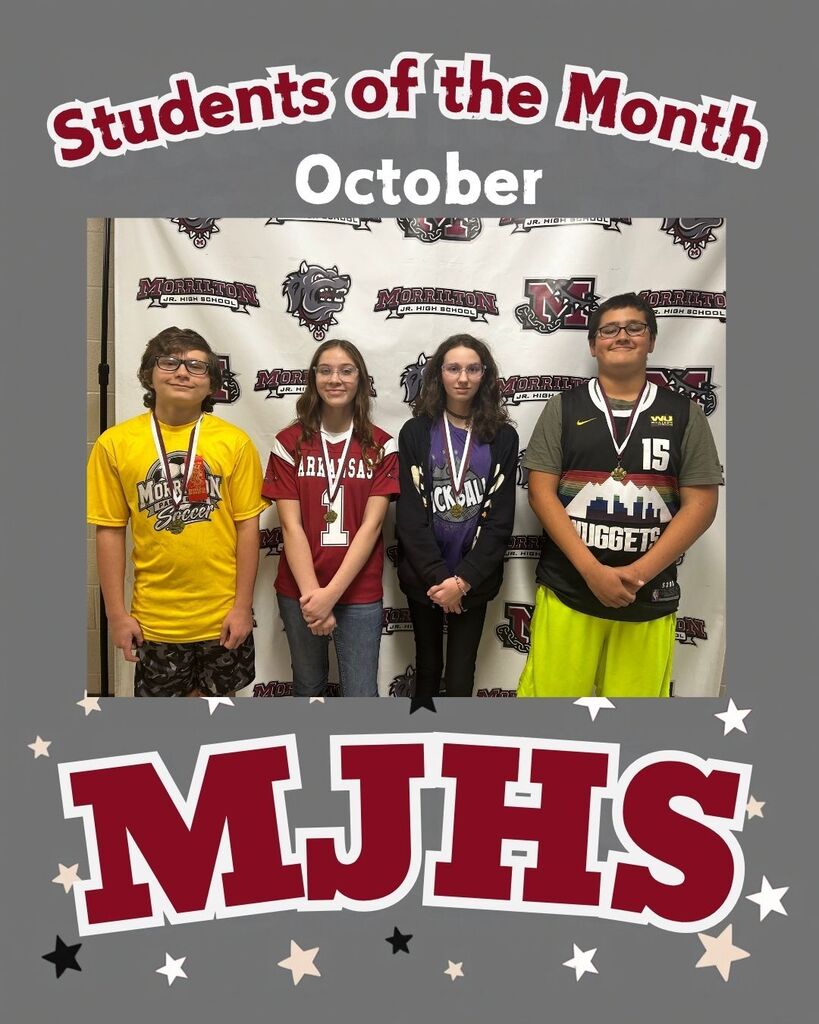 Four students stand together in front of a wall with a printed backdrop. Each student wears a lanyard with a number and a medal. The background reads "Students of the Month October" and "MJHS" with stars.