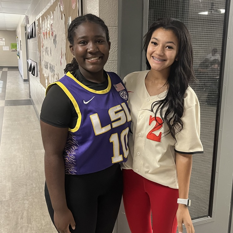 Two girls standing in a hallway, one wearing a jersey with LSU and the other in a white shirt.