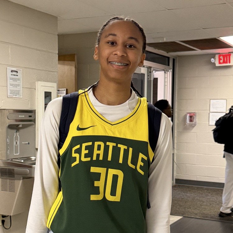 Person in yellow and green jersey with Seattle and 30 smiles in hallway next to sink.