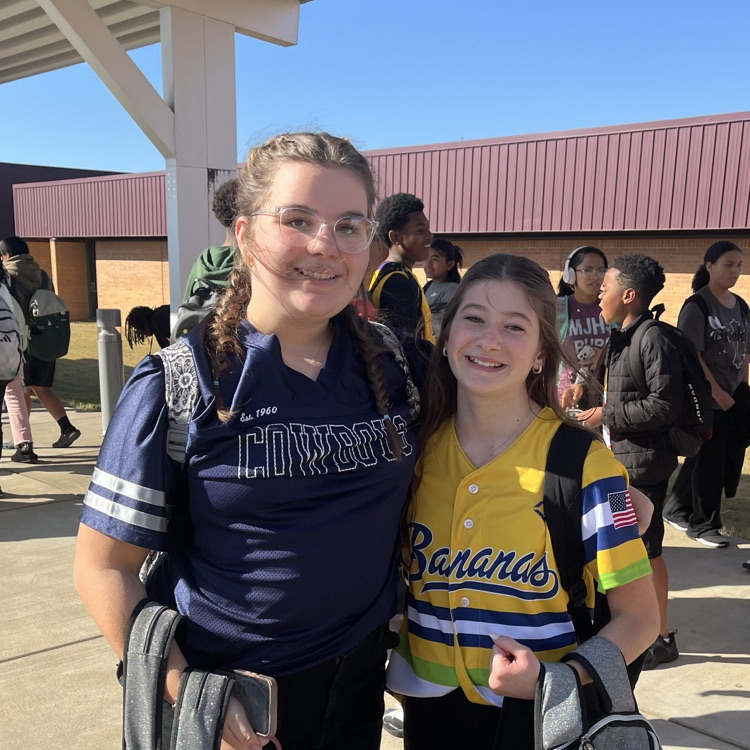 Two students stand together, one wearing a blue shirt with "Cowboys" and the other in a yellow and green shirt with "Baranus."