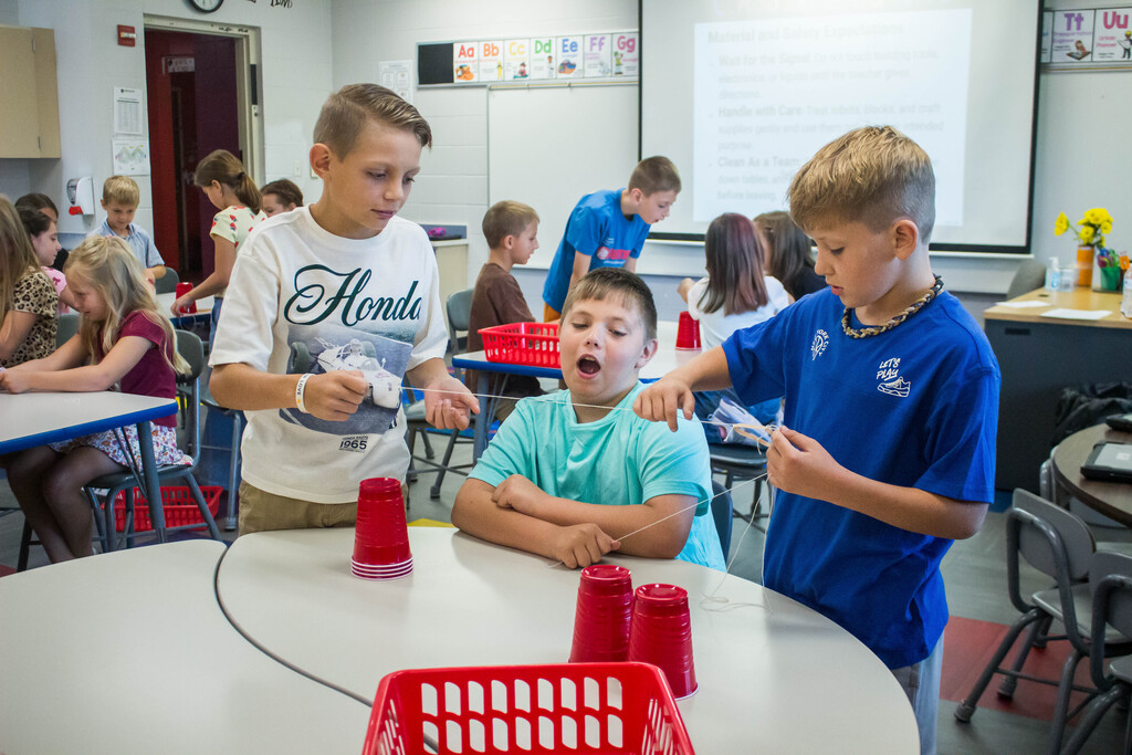 AES  students attempt cup stacking through string.