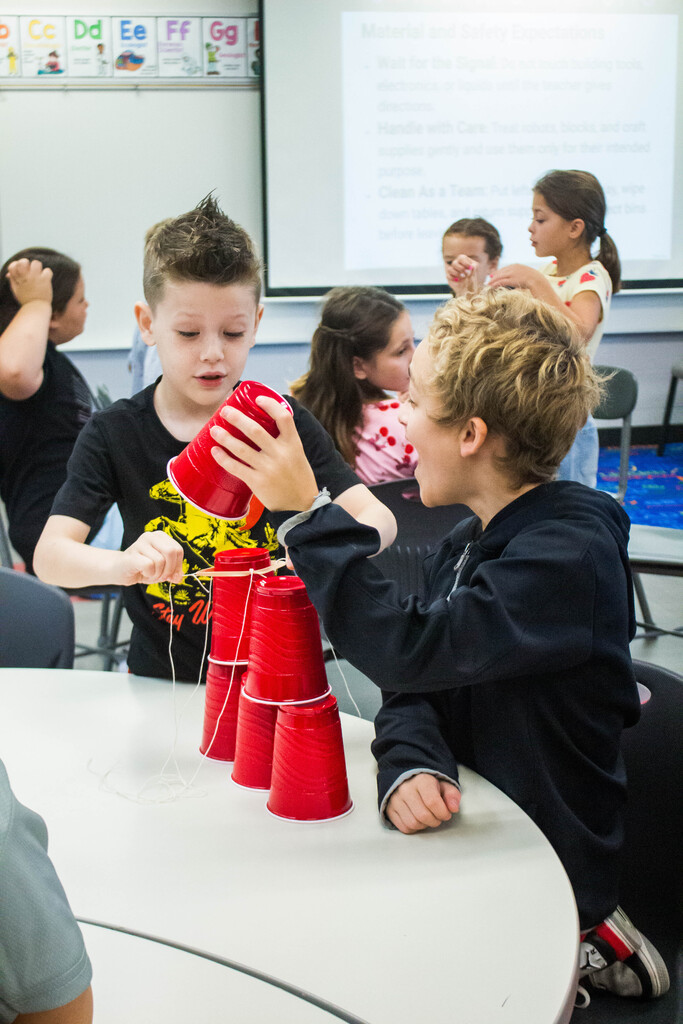 AES  students attempt cup stacking through string.