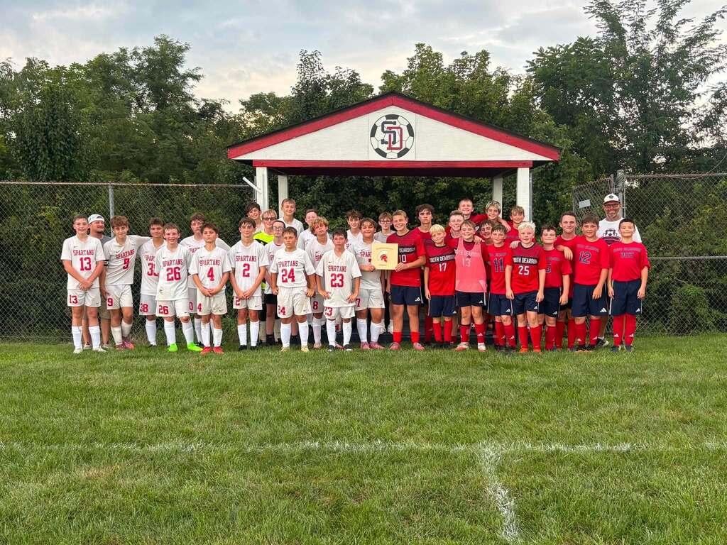 SDMS and CMS soccer teams stand for a photo with the plaque presented.