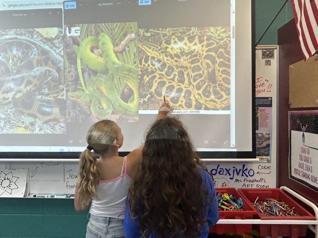 Two Aurora Elementary students pointing to projected anaconda reference photos during a South America art lesson.