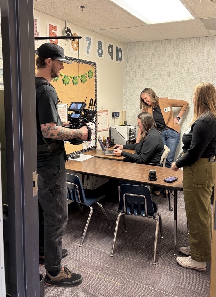 two people looking at computer with film crew in a small classroom