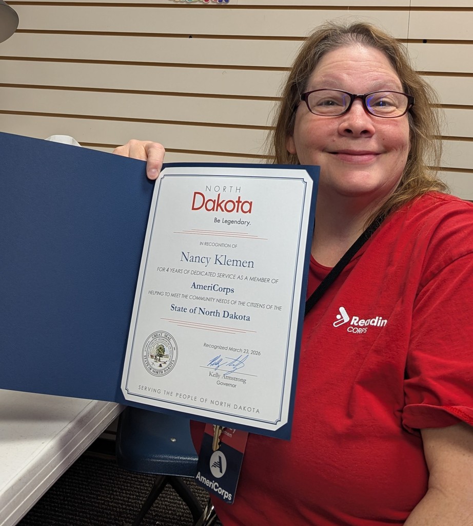 picture of reading corps tutor holding up a certificate from the state of north dakota in recognition for four years of dedicated serve as a member of AmeriCorps signed by the North Dakota governor