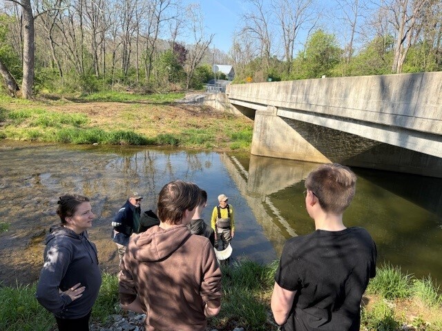Adults and students standing near a bridge over Muddy Creek in preparation for stocking trout.