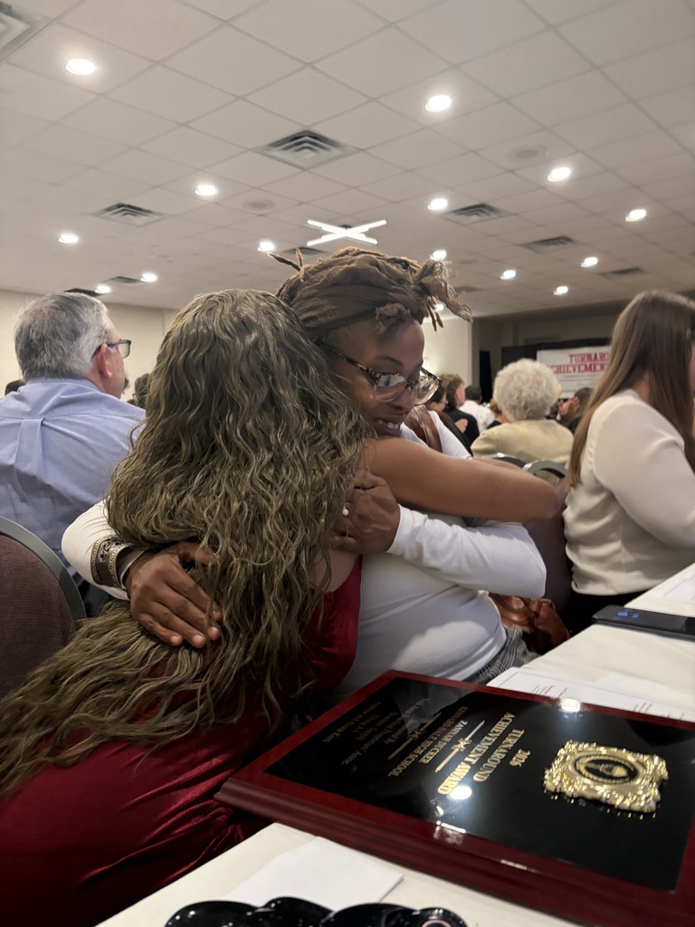 Student receiving a hug of congratulations from an adult for her award.