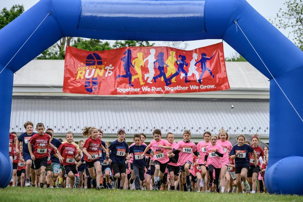 Group of elementary students starting their 5K under the banner "Kids on the Run - Together We Run, Together We Grow"