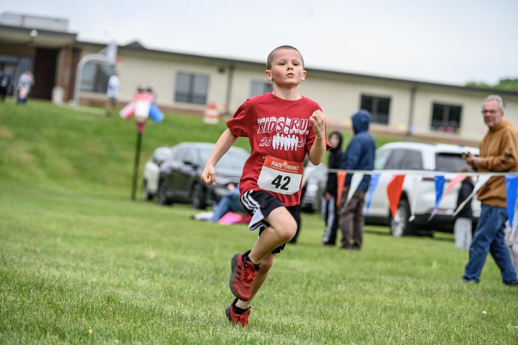 A student running the Kids on the Run 5K with Delta Peach Bottom Elementary School in the background.
