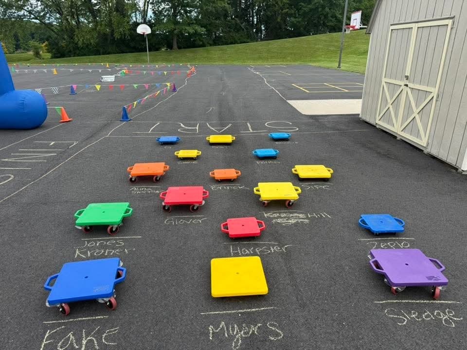 Scooters in multiple colors lined up with chalk names written next to them on the pavement.