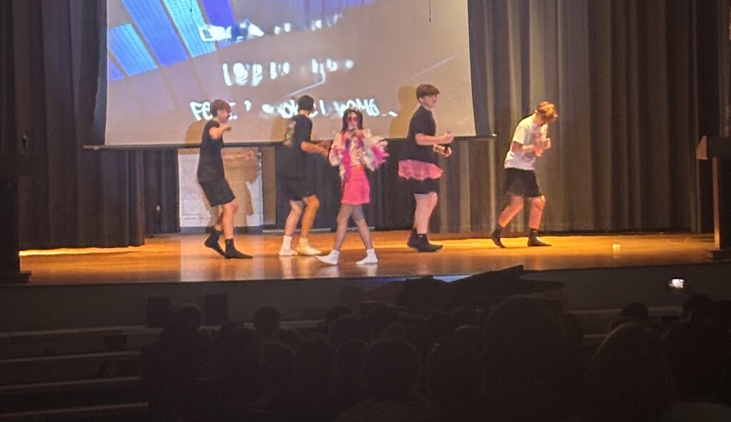 A group of students on stage performing a song and dance routine.