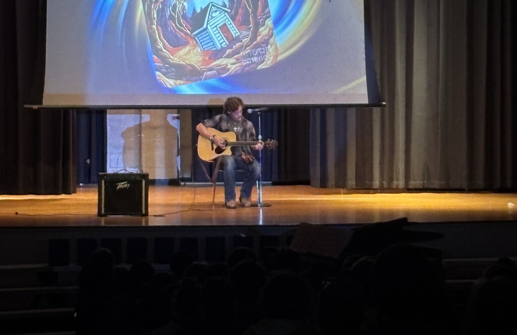 A student on stage performing an acoustic guitar solo.