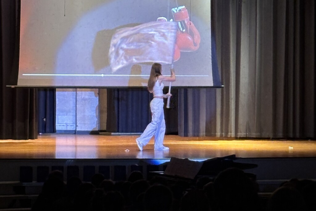 A student on stage twirling a band front flag.