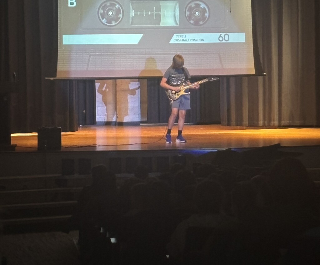 A student on stage performing an electric guitar solo.