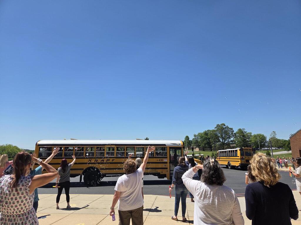 Staff at SEIS waving goodbye and blowing bubbles to students on buses departing campus on the last day of school.