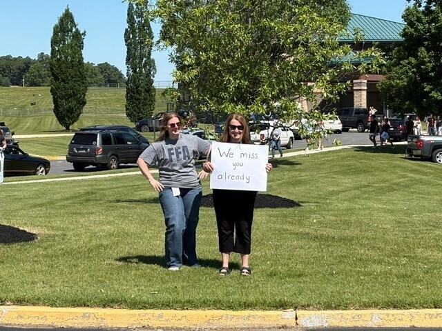 Two teachers holding a sign that says, "We miss you already"