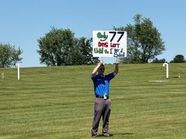 A teacher holding a sign that says, "Only 77 days left until the first day of school"