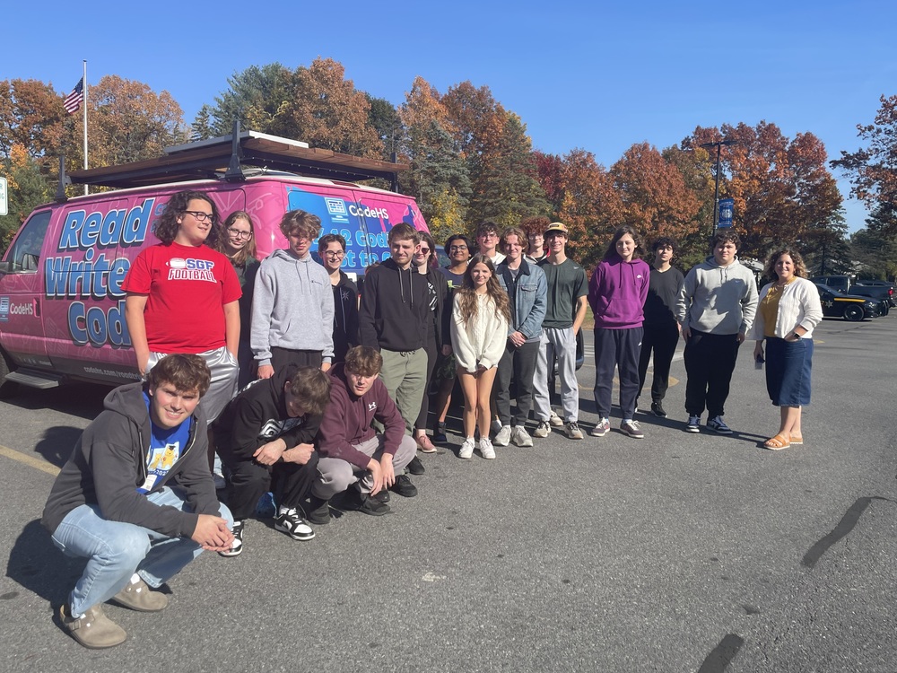 About 20 people pose in front of a pink van