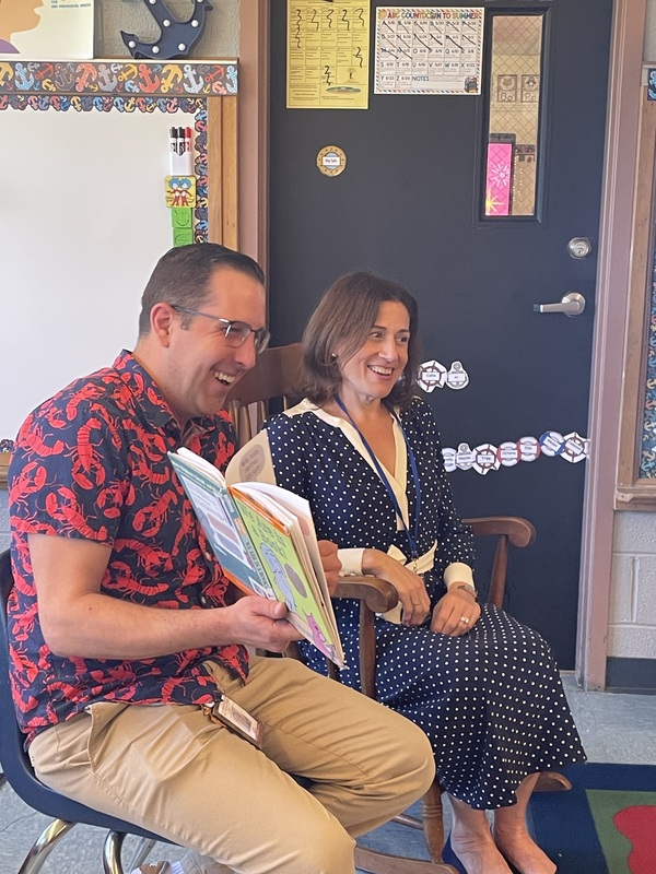 A man in a lobster-print shirt and a woman in a polka-dot dress laugh while looking at a book.
